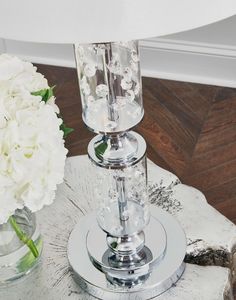 two clear vases with white flowers in them on a table next to a lamp