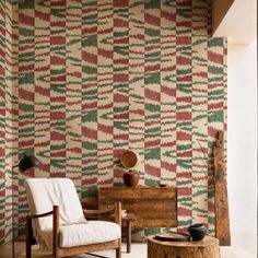 a chair and table in front of a wall with colorful patterns on it, next to a wooden trunk