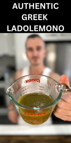 a man holding a measuring cup filled with green liquid in front of him and the words authentic greek ladolemono