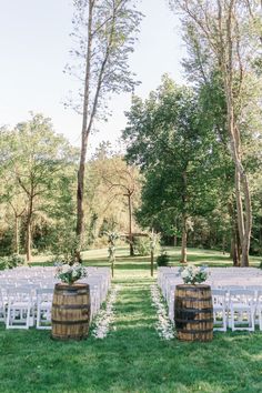 an outdoor ceremony set up with white chairs and wooden barrels on the grass in front of trees