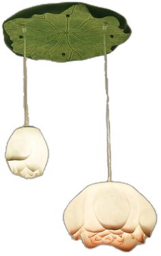 two white objects hanging from the ceiling with green leaves attached to them, one is shaped like a lotus leaf and the other is shaped like a human's head