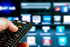 a hand holding a remote control in front of a television screen with blurry background