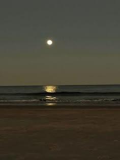 the sun is setting over the ocean and it's reflection in the water on the beach