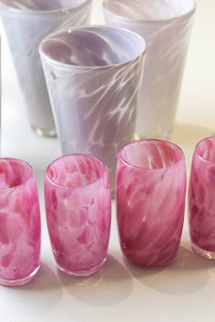 pink marbled glasses lined up on a white table top with one candle in the middle