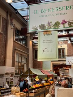 people shopping at an open air market with signs hanging from the ceiling above them that read i benessere per te la tuca casa