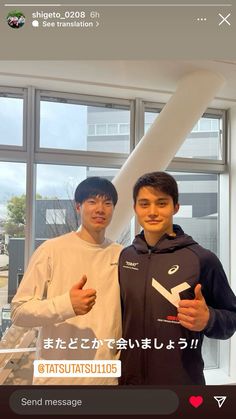 two young men standing next to each other in front of a window holding thumbs up