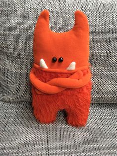 an orange stuffed animal sitting on top of a gray couch with its arms wrapped around it's neck