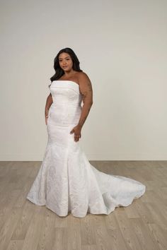 a woman in a white wedding dress standing on a wooden floor with her arms behind her back