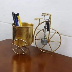 a golden metal cup with pens and pencils in it sitting on a table next to a bike