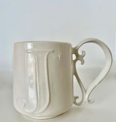 a white coffee cup sitting on top of a table next to a vase with a heart shaped handle