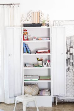 a white bookcase sitting next to a window in a room filled with books and other items