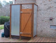 a wooden shed sitting on top of a wooden floor next to a brick wall and potted plant