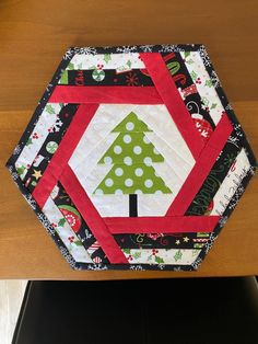 a quilted table topper with a christmas tree in the center on a wooden table