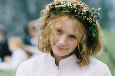 a woman with a flower crown on her head and people in the back ground behind her