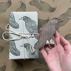 a hand holding a wrapped gift with two birds on it