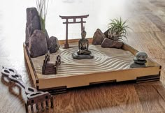 a wooden tray with rocks and plants in it on top of a wood floor next to a brush