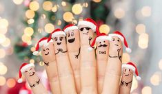 fingers with faces drawn on them and santa's hats around the fingers, in front of a christmas tree