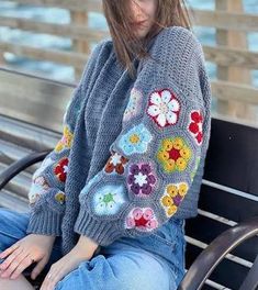 a woman sitting on top of a bench wearing a sweater