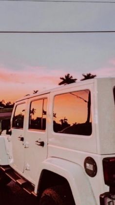 a white jeep parked on the side of a road at sunset with palm trees in the background