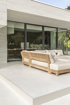 a large wooden couch sitting on top of a white floor next to a building with glass doors