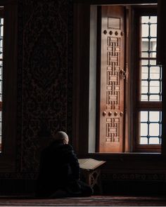 a person sitting on the floor in front of two windows reading a book with an intricate design