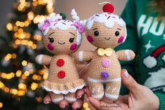 two small crocheted dolls are held in front of a christmas tree with lights