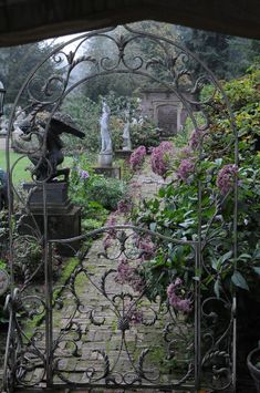 an iron gate in the middle of a garden filled with flowers and statues, surrounded by greenery