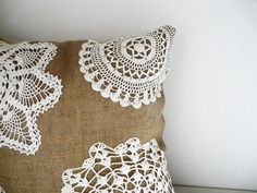 a pillow with white crochet doily on it sitting next to a wall