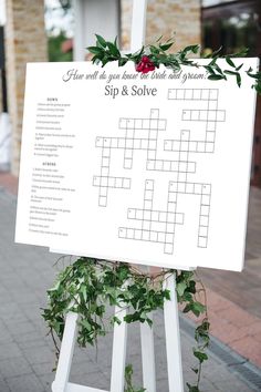 a crossword sign with greenery on it in front of a brick building and sidewalk