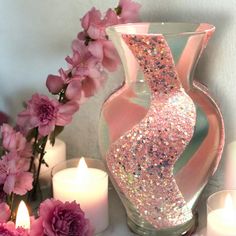 pink flowers and candles sit next to a glass vase with glittery designs on it