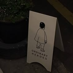 there is a sign that says ordinary heroes next to a potted plant on the sidewalk