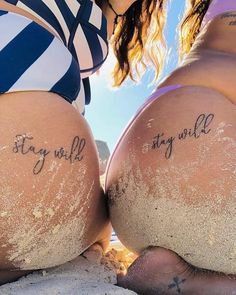 two women sitting on the beach with their butts covered in sand and writing that says stay wild