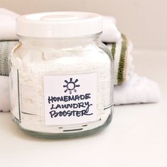 a glass jar filled with laundry powder sitting on top of a white counter next to folded towels