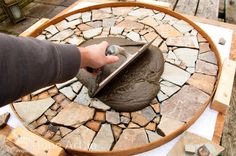 a person using a trowel to cut stone on a circular table with scissors