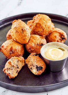 some muffins on a black plate with a small cup of cream cheese sauce