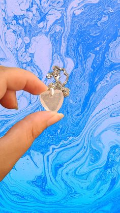 a hand holding a piece of jewelry in front of blue and white swirly background