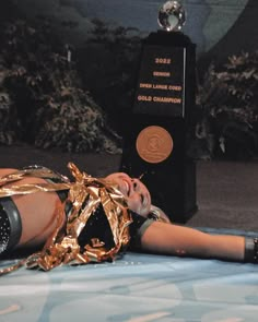 a woman laying on top of a bed next to a trophy and gold ribbon around her neck