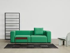 a green couch sitting next to a white chair on top of a black and gray rug