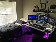 a bedroom with two computer monitors, a bed and a desk in front of a window