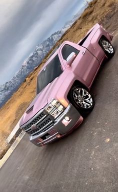 the pink truck is parked on the side of the road in front of some mountains