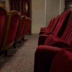 rows of red velvet seats lined up against a wall in a room with carpeted flooring