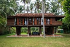 a large wooden house sitting on top of a lush green field next to palm trees