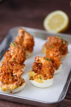 small deviled eggs with meat and cheese on a tray next to lemon wedges