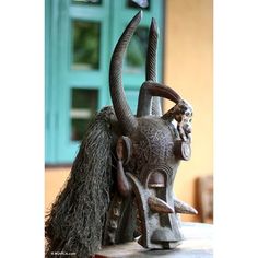 a statue of an animal with long horns and hair on it's head sitting on a table in front of a door