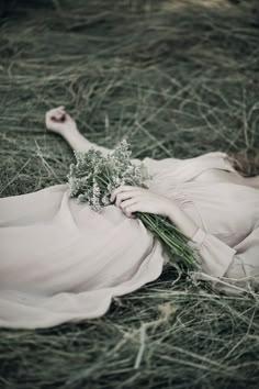 a woman laying on the ground with flowers in her hand and wearing a long white dress