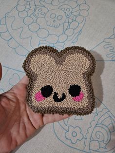 a hand holding a small piece of crocheted material with a bear face on it