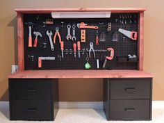 an organized tool cabinet with tools on the wall and drawers below it, in front of a brown wall