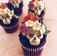 three cupcakes decorated with flowers and skulls on top of each other, sitting on a table