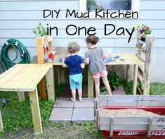 two young children standing at a table made out of wooden pallets with the words diy mud kitchen in one day