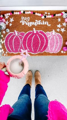 a person standing in front of a door mat with pumpkins on it and pink pom poms